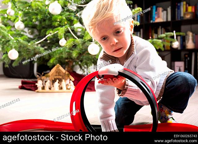 Boy playing with his Christmas present, a plastic racetrack in front of the Christmas tree