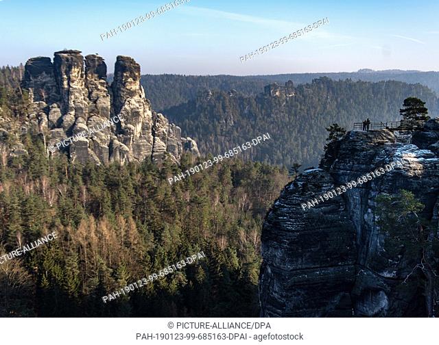 23 January 2019, Saxony, Lohmen: Two tourists look at the rock formations in the Saxon Switzerland National Park from a vantage point