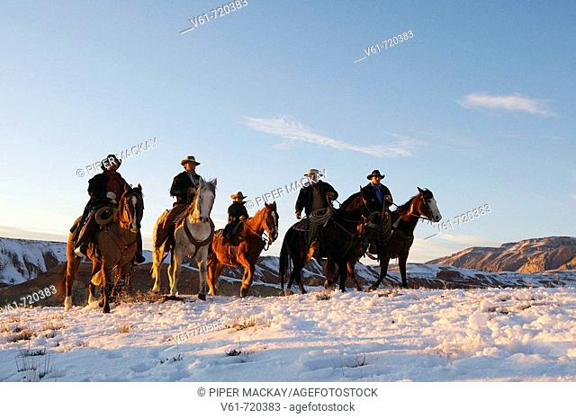 Wranglers leading their horses over the snowcaped ranges of wyoming at sunset