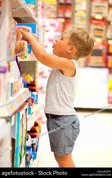 Little boy choosing toys on the high shelf in the shop