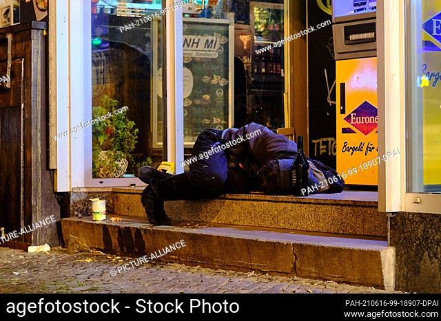 14 June 2021, Berlin: A homeless man sleeps curled up on a staircase on Kottbusser Damm in the Kreuzberg district next to a bottle with an alcoholic drink