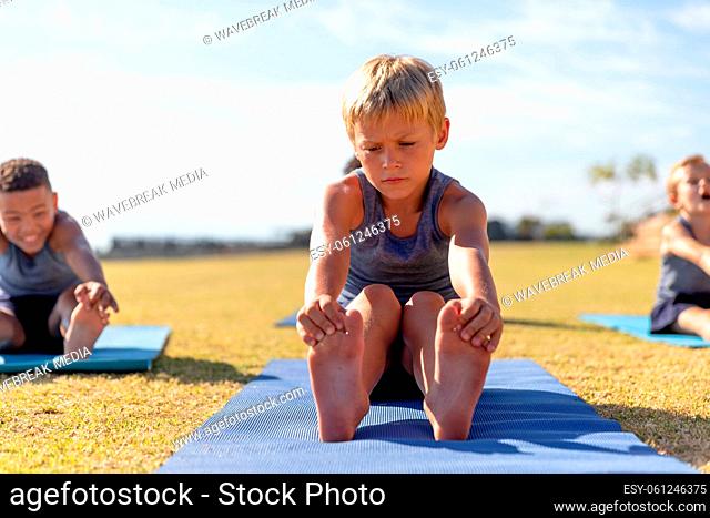 Multiracial elementary schoolboys touching toes while exercising on yoga mat in school ground