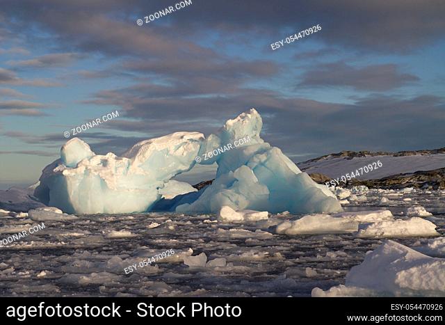 small iceberg in Antarctic waters clogged with ice against a rocky shore