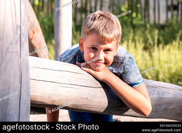 Blond boy smiling and looking at the camera while sitting on wooden playground in a public park