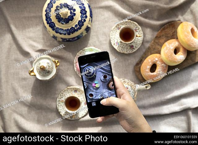 Top view picture of lady, blogger sitting in cafe and making photo with mobile of food, afternoon tea with doughnuts and macarons on the table high angle