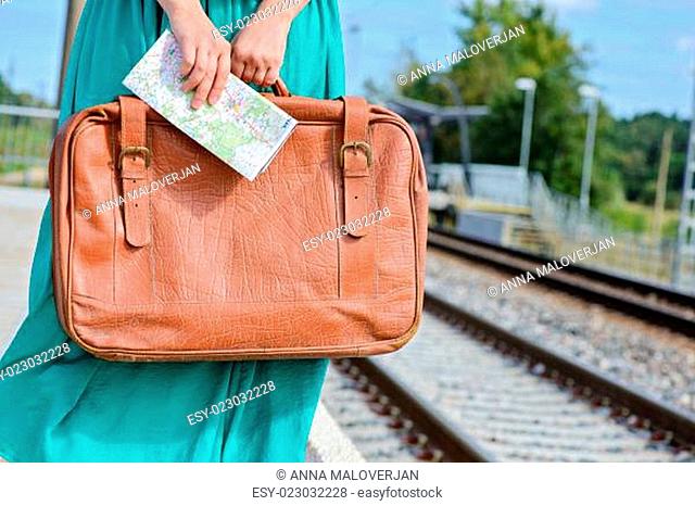 Womans hands holding a map and suitcase at station