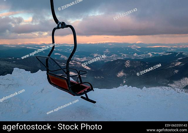 Alpine resortr ski lift with seats going over the sunset mountain skiing slopes in extremally windy weather