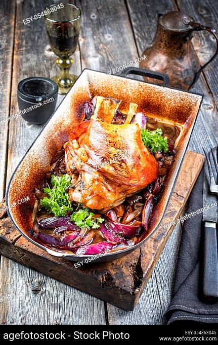 Traditional Bavarian schweinshaxe with onion as closeup in a rustic stewpot on an old wooden board