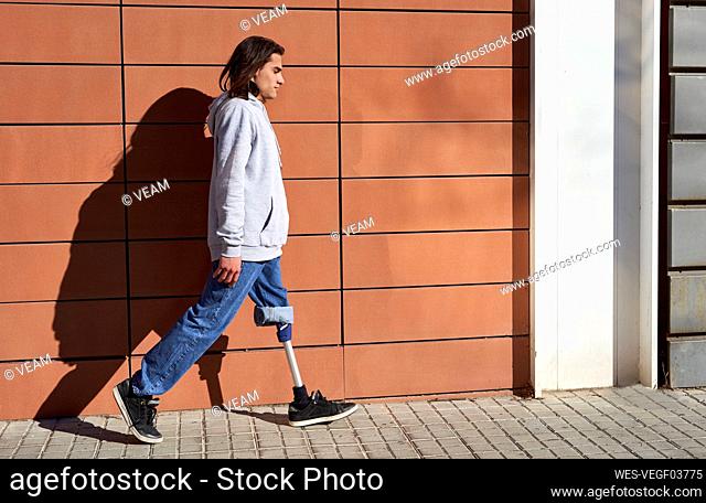 Young man with prosthetic leg walking by wall during sunny day