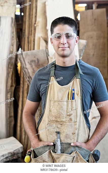 View of a young Caucasian man factory worker wearing an apron in a woodworking factory