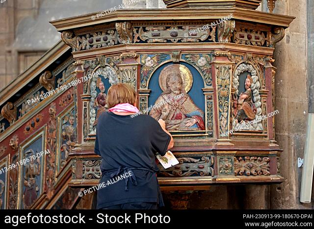 13 September 2023, Saxony-Anhalt, Halberstadt: Restorer Christine Machate is repairing spots on a pulpit relief in Halberstadt Cathedral