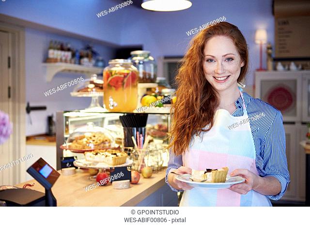 Portrait of smiling young woman serving cake in a cafe