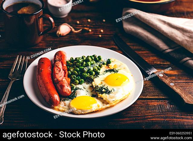 Breakfast with fried eggs, sausages and green peas on white plate