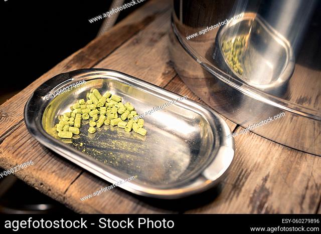 Hop pellets lying in stainless steel tray on wooden floor ready to be put into the wort while brewing beer in garage at home