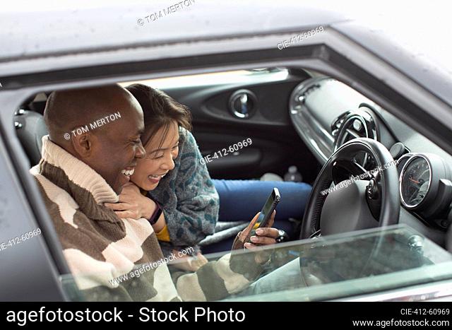Happy couple using smart phone in car window