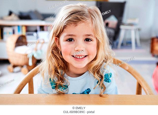 Portrait of young girl, sitting at table, smiling