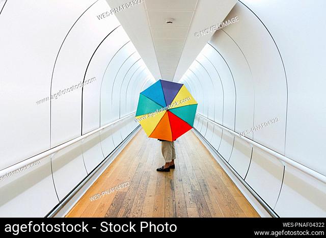 Young woman with multi colored umbrella standing on walkway