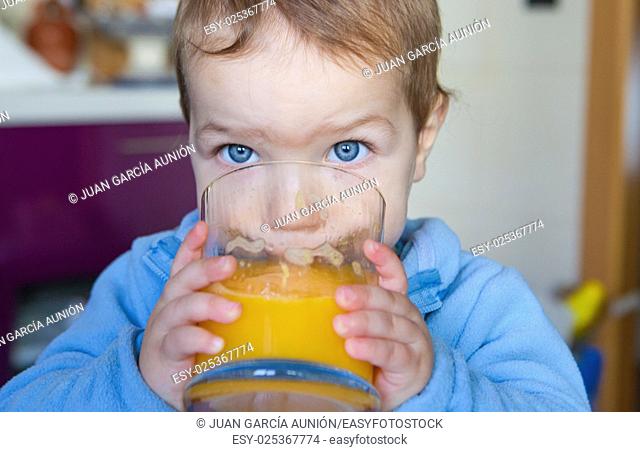 Baby boy drinking a big glass of orange juice fresh made. Education on healthy nutrition for children concept