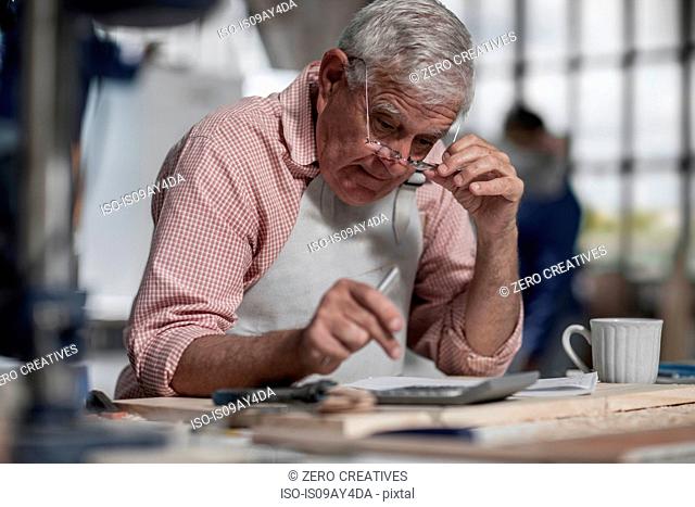 Senior carpenter using calculator in wood workshop