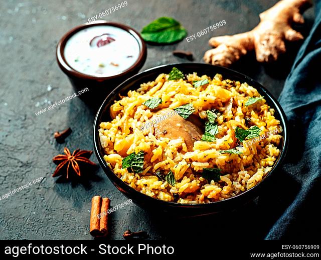 Pakistani food - biryani rice with chicken and raita yoghurt dip. Delicious hyberabadi chicken biryani on black background
