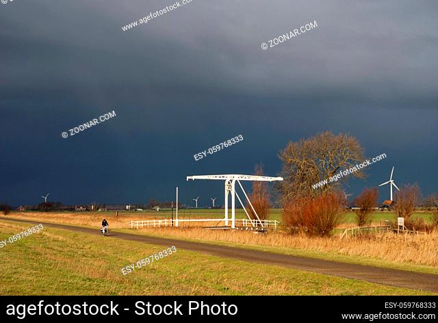 Cyclist tries to stay ahead of a heavy shower on a bicycle path in the Dutch province Friesland