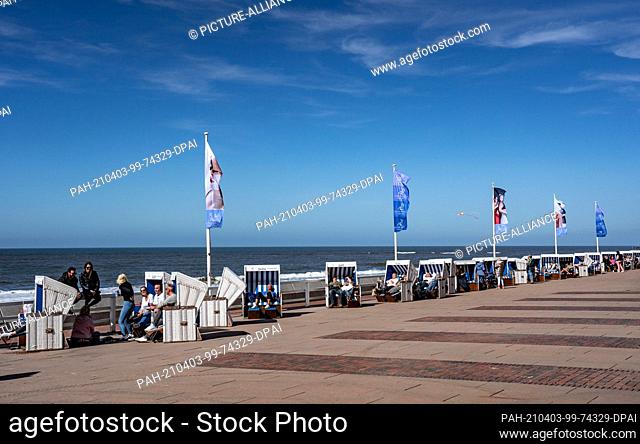 03 April 2021, Schleswig-Holstein, Westerland/Sylt: People sit on the beach promenade in Westerland on Holy Saturday. Photo: Axel Heimken/dpa