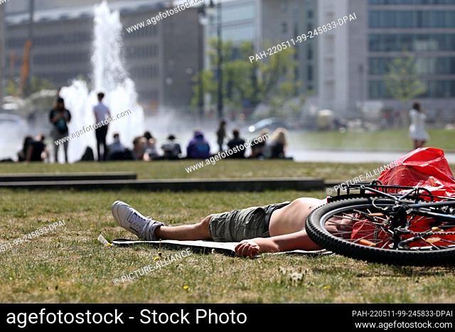 11 May 2022, Berlin: A man has laid down on the grass next to his bicycle in the Lustgarten in temperatures around 25 degrees Celsius and is enjoying the warm...