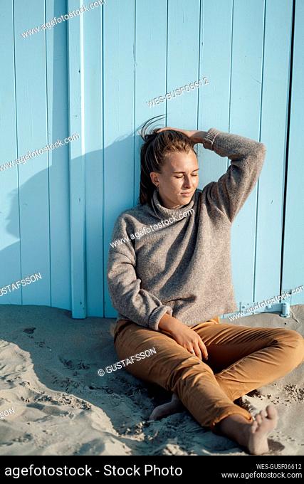 Young woman with head in hand sitting by blue door at beach on sunny day