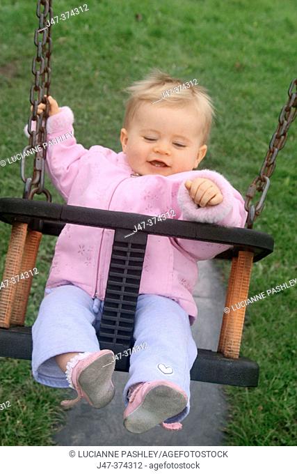 10 month old baby girl swinging in park smiling