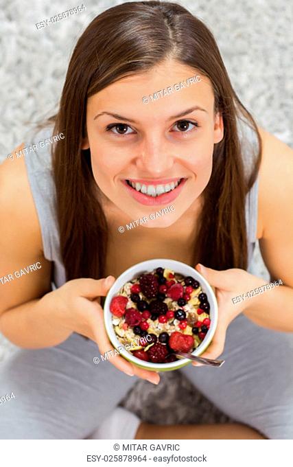 Happy young woman holding cereal muesli with fruits in bowl at home. Healthy Food and Dieting concept