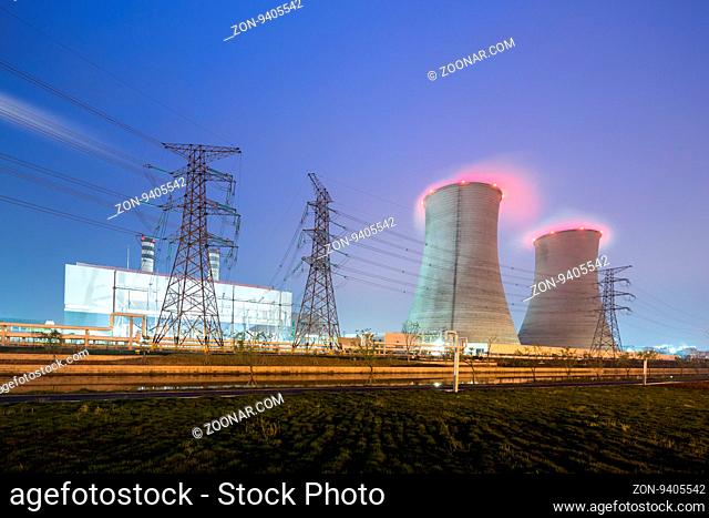 cooling towers with red smoke and pylons in modern power plant at twilight
