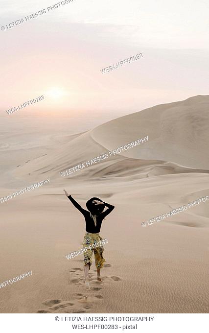 Namibia, Namib, back view of fashionable woman jumping on desert dune