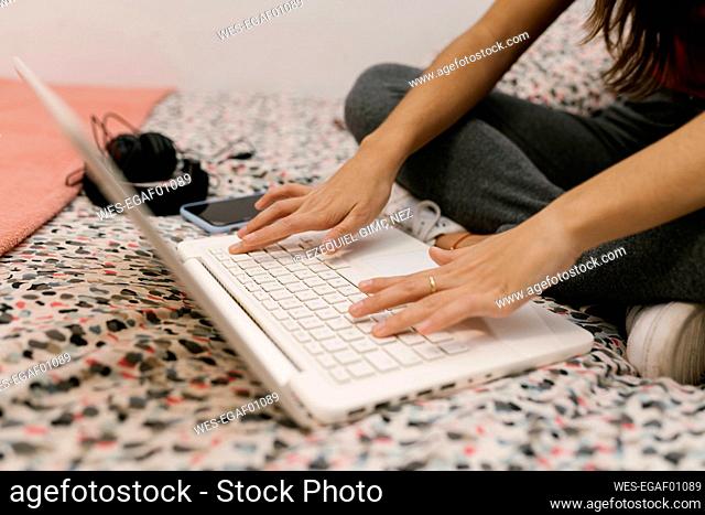 Teenage girl trying on laptop while sitting on bed