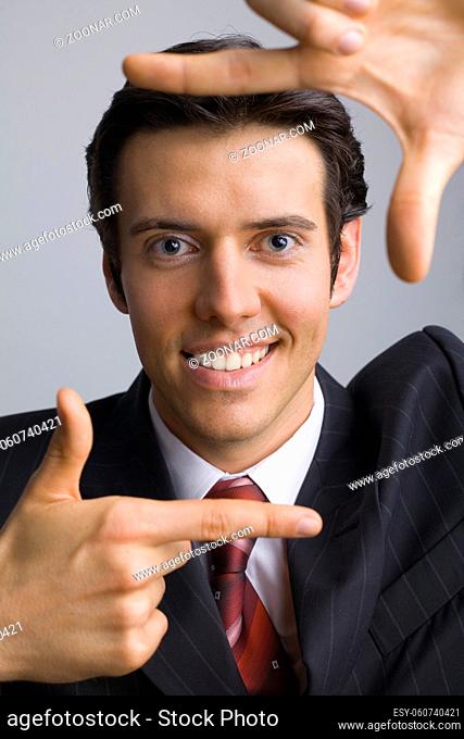 Smiling, handsome businessman. Showing his face by hands. Looking at camera. Gray background, front