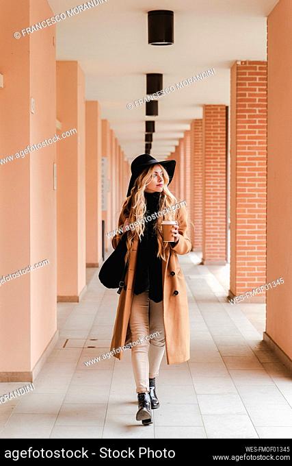 Young woman with reusable coffee cup walking through corridor