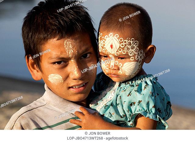 Myanmar, Mandalay, Lake Taungthaman. A young girl and boy with elaborate Thanaka face decoration by U Bein Teak Bridge in Myanmar