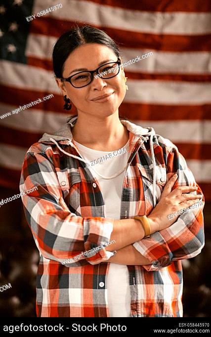 Intelligent American Gleefully Smiles With Her Arms Crossed Amid America's Striped Flag, The Patriotic Brunette Woman Celebrates Her Country's Independence And...
