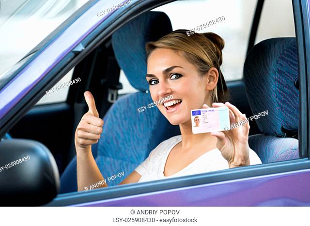 Portrait of excited young woman showing license while sitting in car