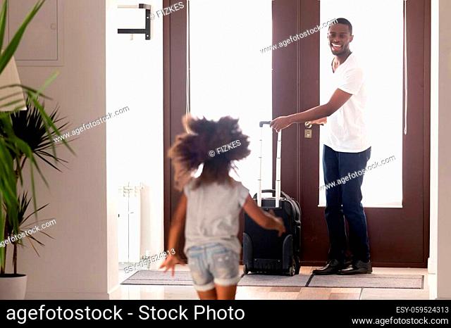 Rear back view small african daughter running to meet beloved loving father returned arrived from travel business trip standing in doorway with luggage baggage