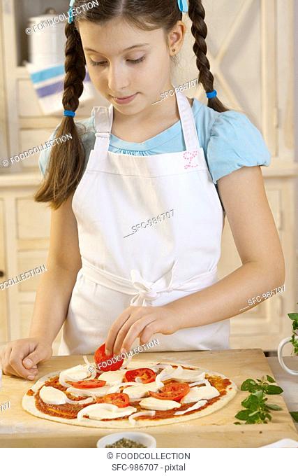 Girl putting tomatoes on pizza