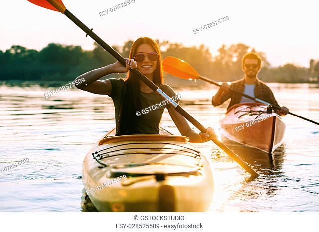 Enjoying river adventure. Beautiful young couple kayaking on river together and smiling