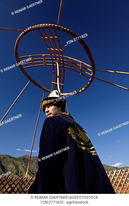 Man in traditional clothes holding up the wood roof crown for a yurt in Saty Kazakhstan