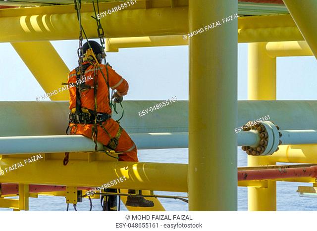 Working at height. An abseiler from side view with dirty coverall wearing Personal Protective Equipment (PPE) hanging at life lines to remove dents at pippeline...