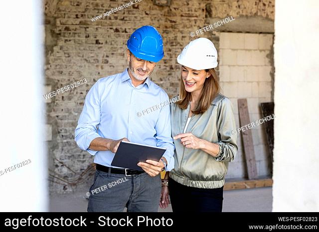 Female client and male architect wearing hardhats while discussing over digital tablet at construction site
