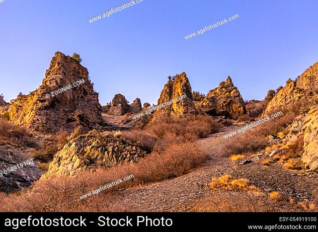 Jagged and rocky mounds on the side of a mountain. Sunset light hitting the side of the mountain seen from below looking up in Provo Canyon on a trail called...