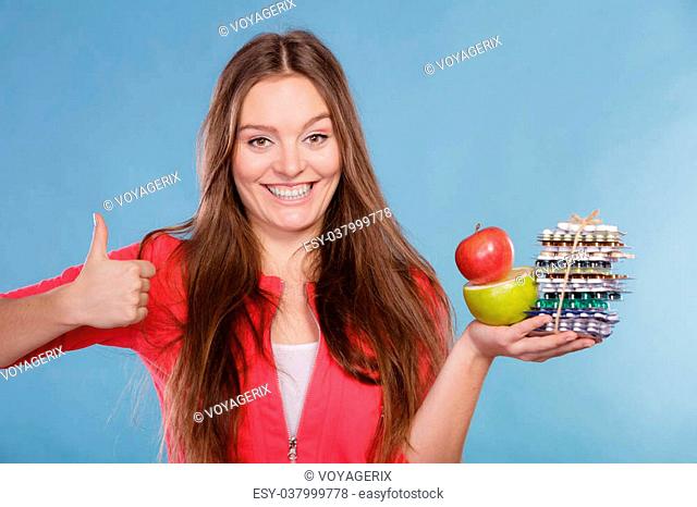 Woman girl with thumb up holding vitamin tablets pills and fruits. Choice between natural and synthetic vitamins. Health care
