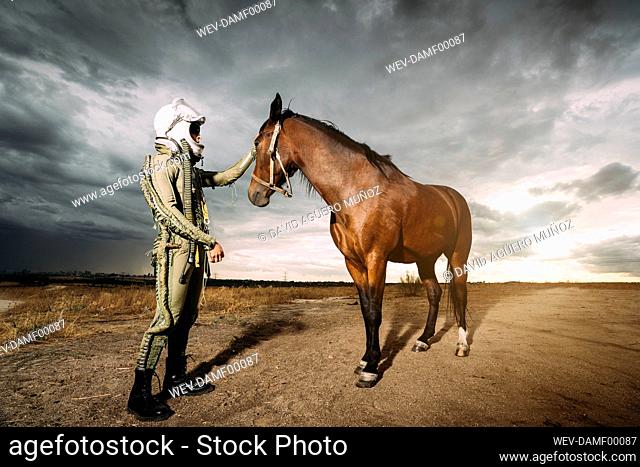 Man dressed as an astronaut with a horse on a meadow with dramatic clouds in the background