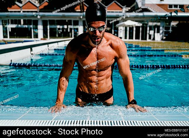 Muscular male swimmer getting out from swimming pool on sunny day