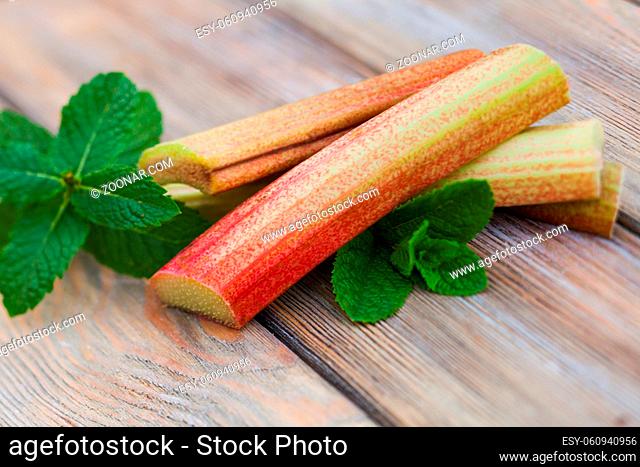 Fresh rhubarb and mint leaves on a wooden table close up