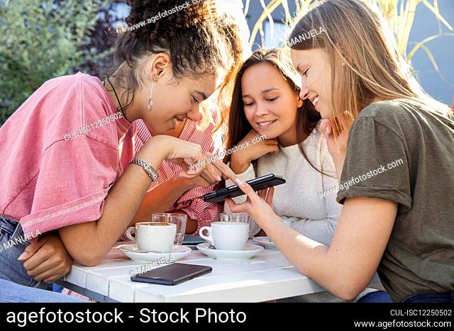 Three women sitting round a table looking at a mobile phone and smiling